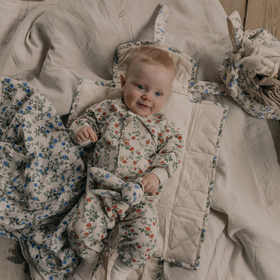 baby laying on a blanket and change to go in a flower printed jersey onesie