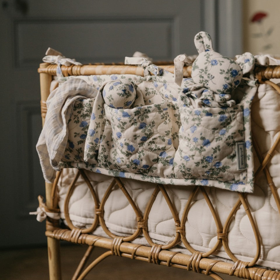 Wicker crib with floral-patterned baby blanket and toys against a neutral background