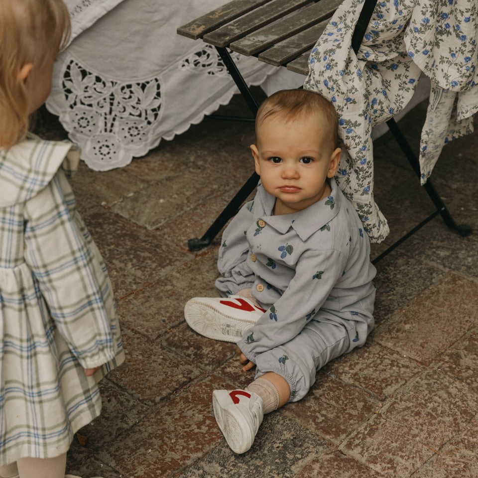 baby sitting on the floor in a blue onesie with a fruit pattern