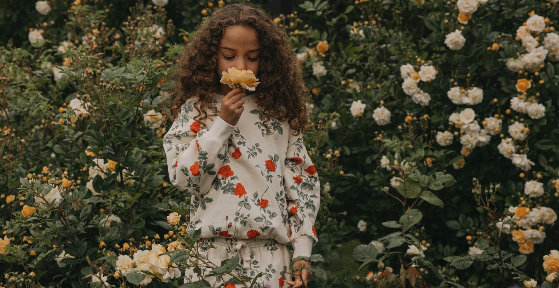 Girl smelling a flower in a flower field. She's wearing a flower sweatshirt