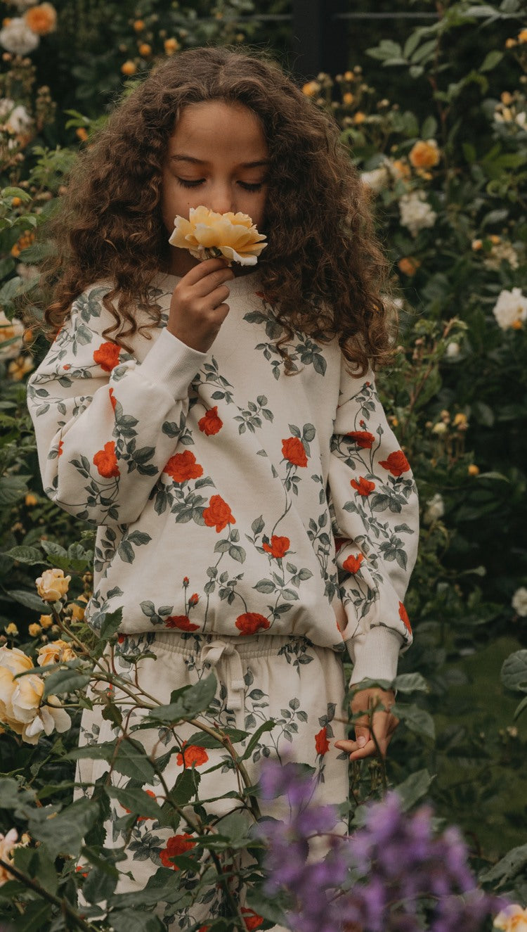 Girl smelling the flower in a flower garden, wearing a flower sweatshirt