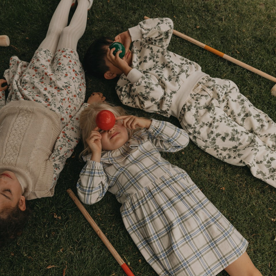 Kids laying on grass holding cricket balls in floral and check patterned clothing