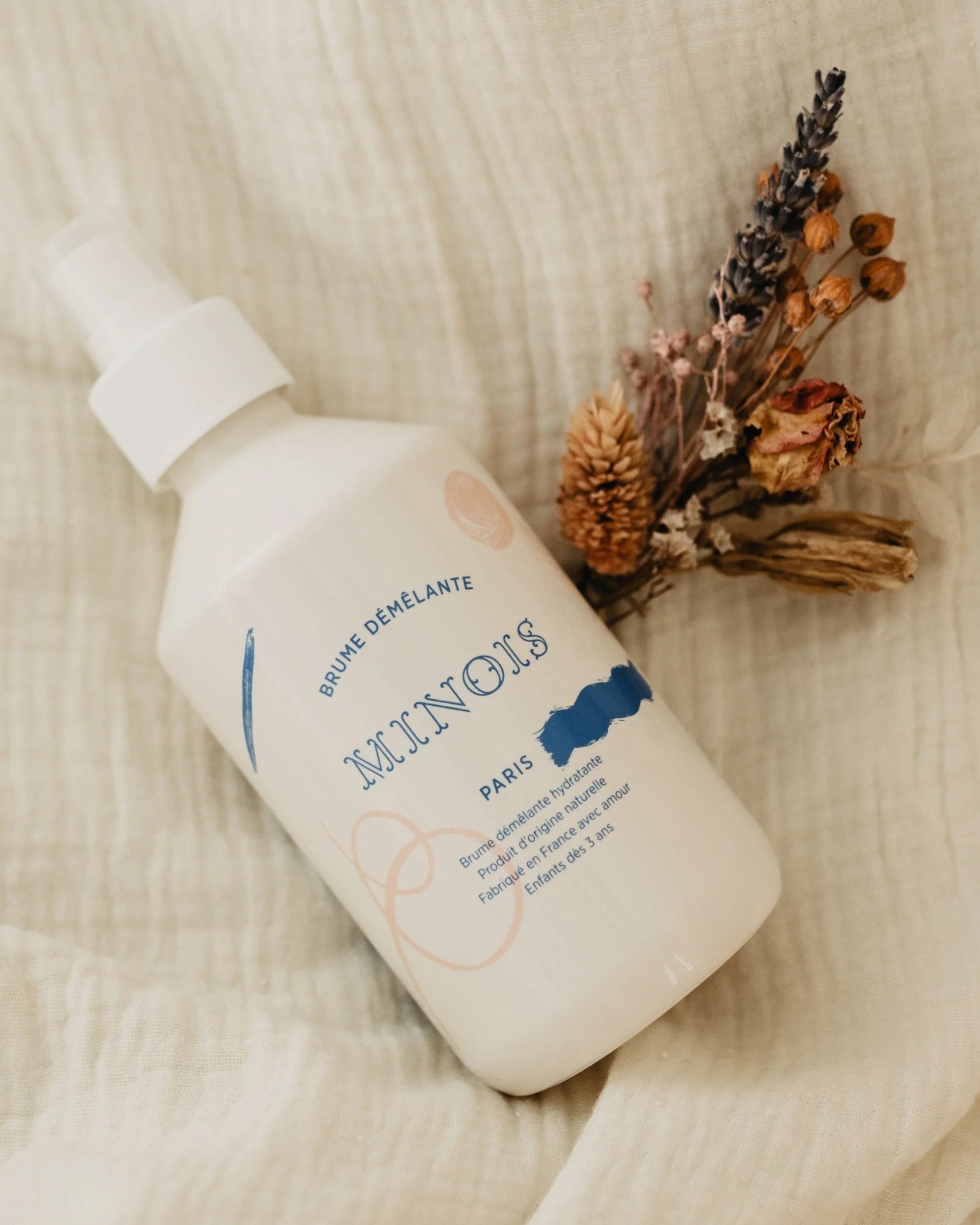 White bottle with 'Minois' branding on a textured beige surface with dried flowers.