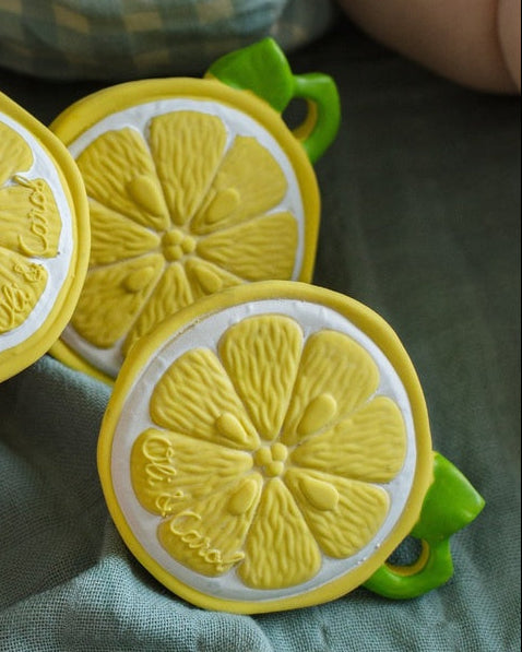 Yellow lemon-shaped teether held by a child's hand on a green fabric background