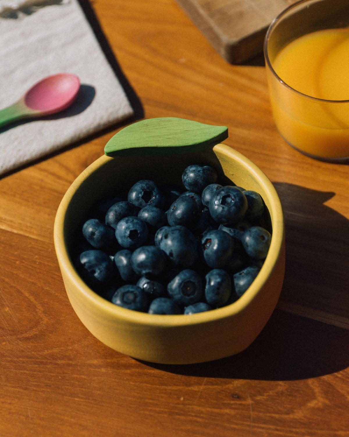 Yellow bowl with blueberries on a wooden table next to a glass of orange juice.