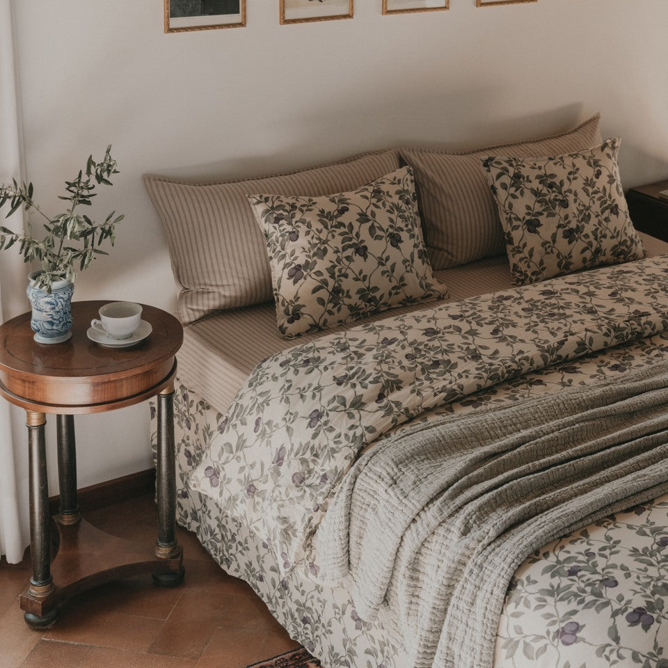 Bed with flower patterned bed linnens with a bed side table next to it. 